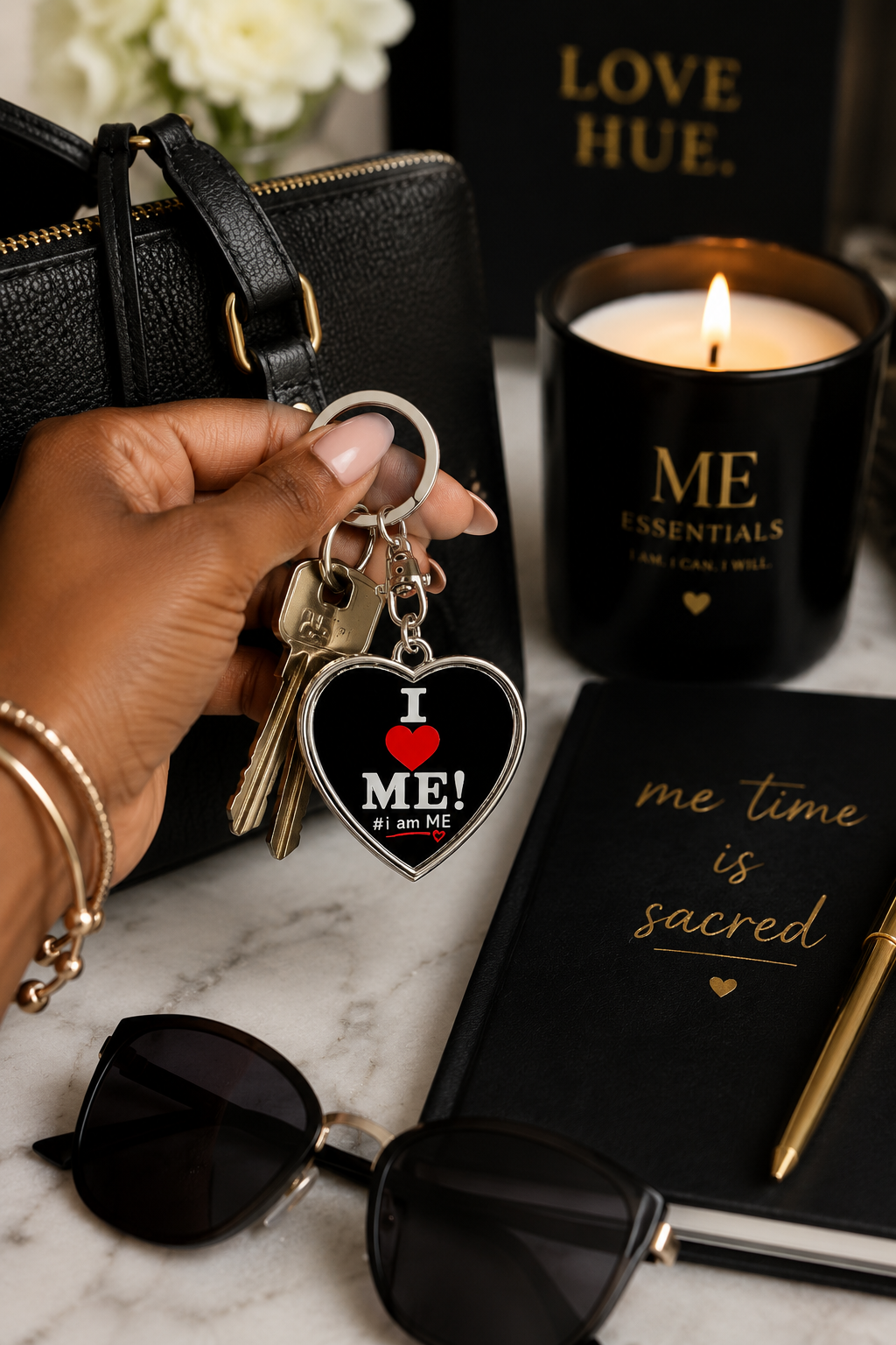 Black woman holding I Love ME heart keychain with candle and self-care essentials on vanity.
