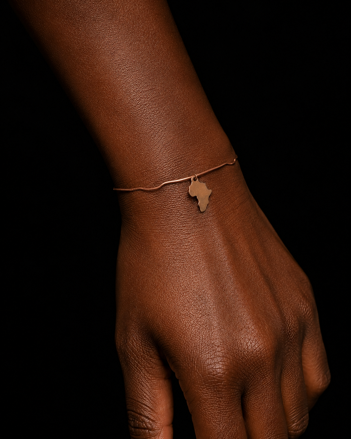 Close-up of a Melanin Copper Cuff with a gold-plated Africa charm worn on a dark-skinned wrist against a black background.