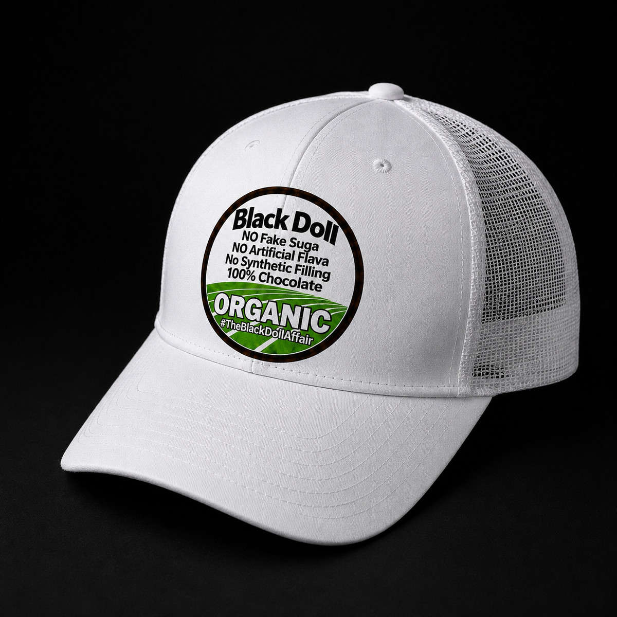 The Black Doll Affair's 'Organic Original' five panel white trucker-style baseball cap with a flat brim, mesh back panels, and a circular front patch reading 'Black Doll' No fake suga, no artificial flava, no synthetic filling, 100% chocolate.' 'ORGANIC' on a black background.