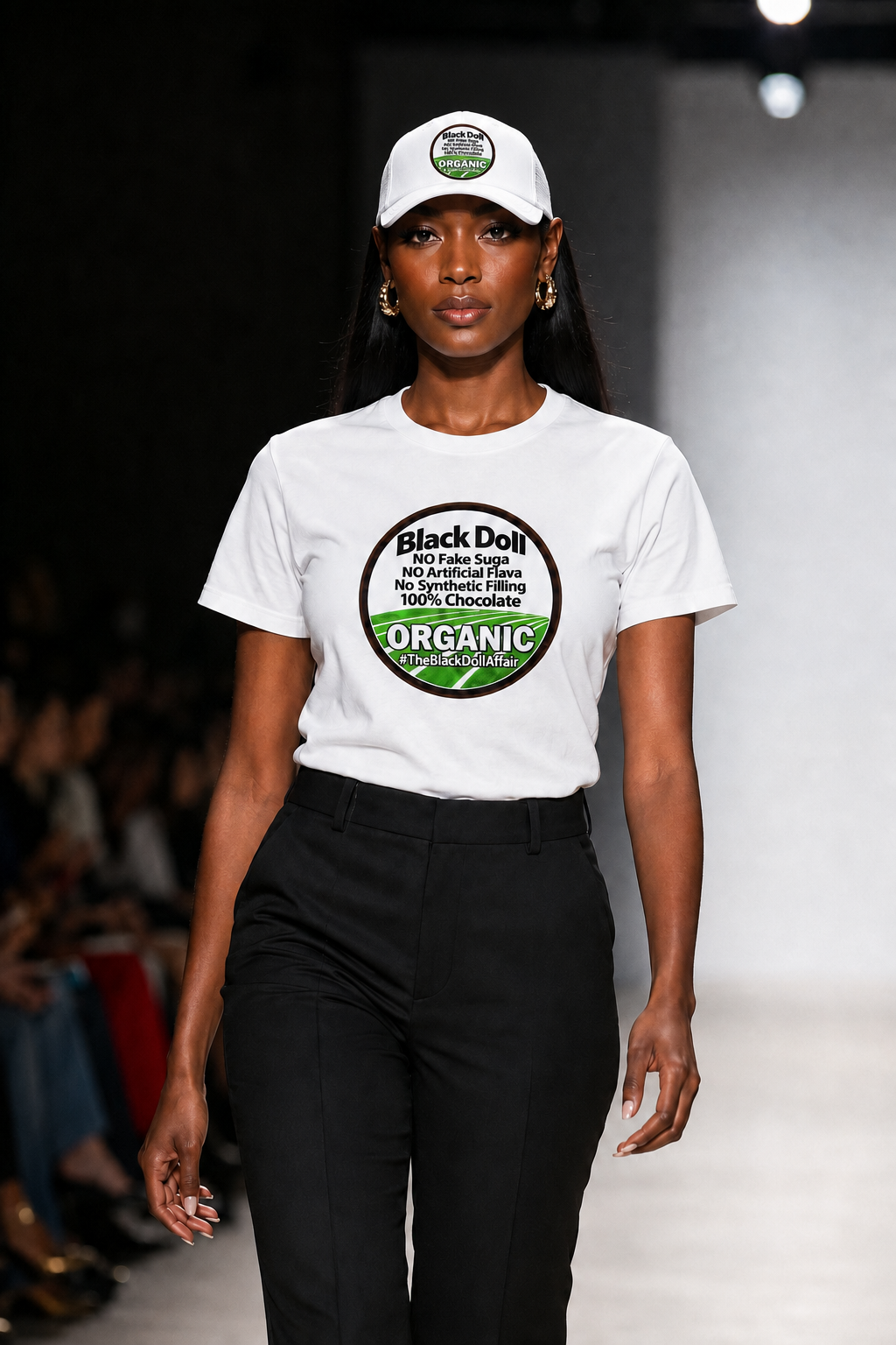 A woman modeling The Black Doll Affair's 'Organic Original' T-shirt and matching five panel white trucker-style baseball cap with a flat brim, mesh back panels, and a circular front patch reading 'Black Doll' No fake suga, no artificial flava, no synthetic filling, 100% chocolate.' 'ORGANIC' on a black background.