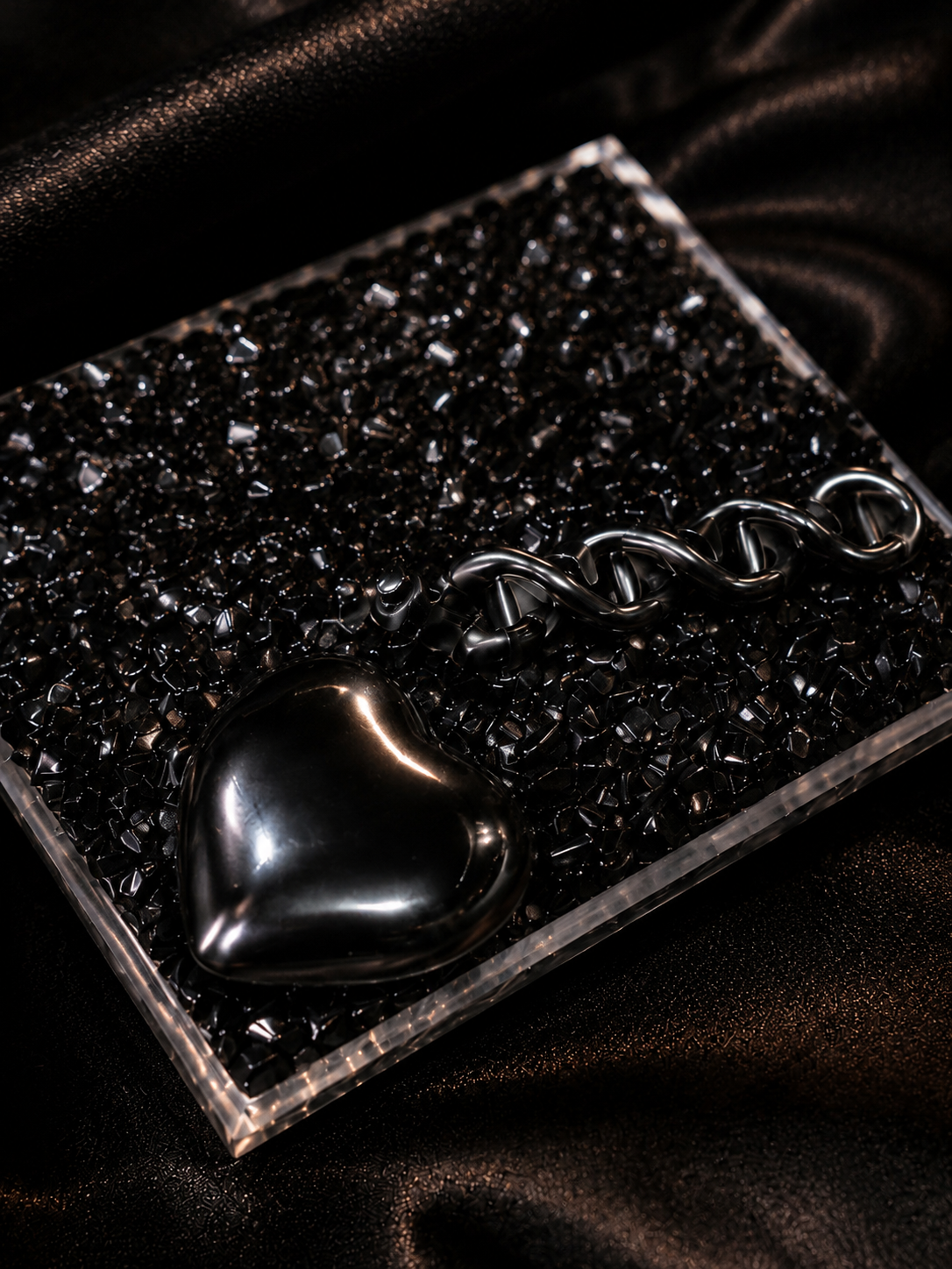 Close-up of the Dark Matter ME Doll™  Display featuring a glossy black heart charm, black DNA helix, and black crystal square case on dark satin background.