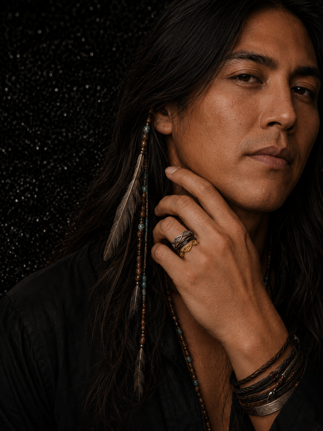 Close-up portrait of a man wearing three Unity Helix Rings™ in black, silver, and gold. Featuring a black loop ring and DNA double-helix designs in gold and silver with layered bracelets and necklaces.